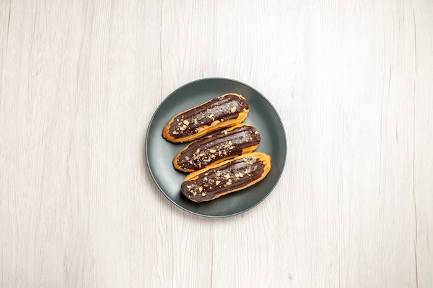 Vista superior de éclairs de chocolate na placa cinza no centro do chão de madeira branco