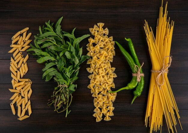 Vista superior de espaguete cru com macarrão de pimenta e um punhado de hortelã em uma superfície de madeira