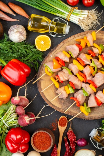 Vista superior de espetos de frango cru em madeira natural tábua de especiarias vegetais na mesa escura