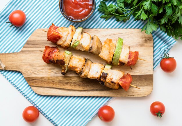 Vista superior de espetos de frango na tábua de cortar com molhos e tomates