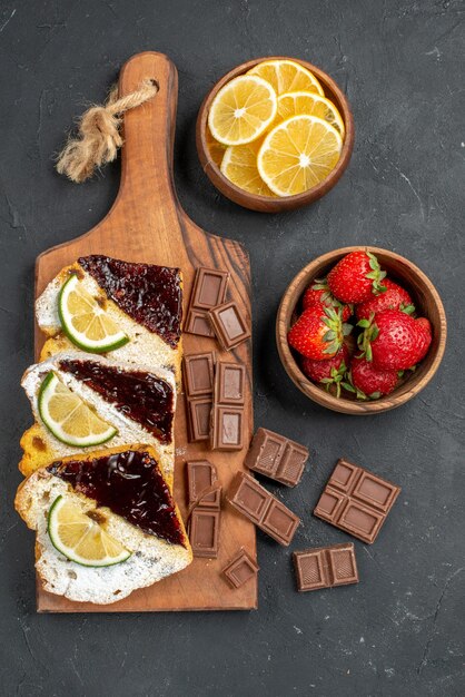 Vista superior de fatias de bolo saborosas com chocolate e frutas na superfície escura