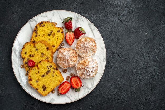 Vista superior de fatias de bolo saborosas com morangos vermelhos frescos e biscoitos em superfície cinza-escura