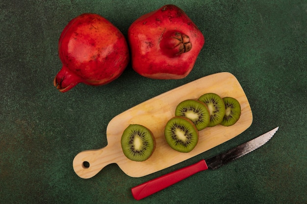 Vista superior de fatias de kiwi na tábua de cortar com romãs e faca na parede verde