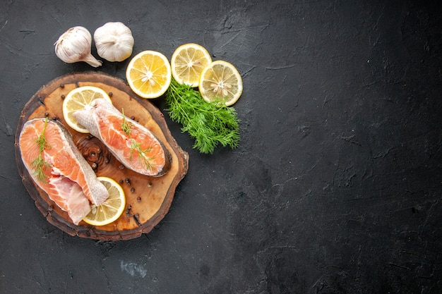 Vista superior de fatias de peixe fresco com rodelas de limão na mesa escura