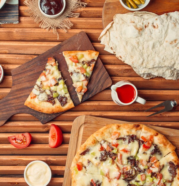 Vista superior de fatias de pizza de carne na tábua de madeira