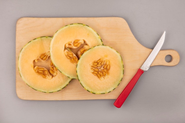 Vista superior de fatias frescas de melão melão em uma placa de cozinha de madeira com uma faca em uma parede cinza