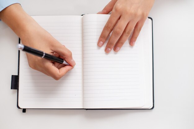 Vista superior, de, femininas, mãos, escrita, em, caderno, escrivaninha