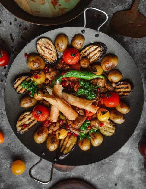 vista superior de frango saj com pimenta, beringela, tomate, batata e pão sírio