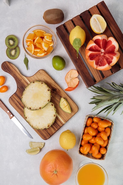 Vista superior de frutas cítricas como abacaxi cortado na tábua e toranja cortada na caixa com limão kiwi laranja com suco de laranja em fundo branco