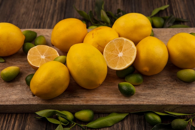 Vista superior de frutas cítricas, como kinkans e limões em uma placa de cozinha de madeira em um fundo de madeira