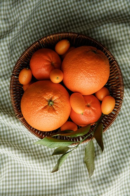 Vista superior de frutas cítricas como tangerina laranja e kumquat na cesta em fundo de pano xadrez