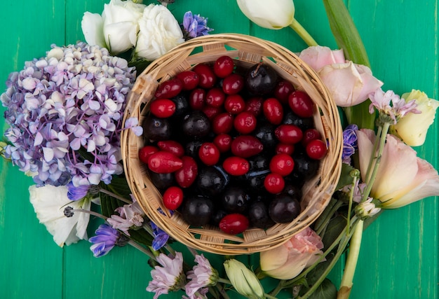 Vista superior de frutas como abrunho e cornel numa cesta com flores ao redor sobre fundo verde