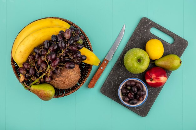 Foto grátis vista superior de frutas como pêra, pêssego, maçã e bagas de uva, limão na tábua e cesta de banana coco uva com faca no fundo azul