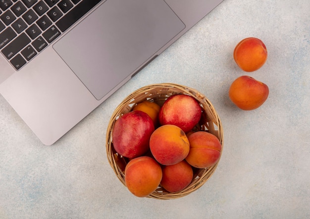Vista superior de frutas como pêssego e damasco em uma cesta com caderno no fundo branco