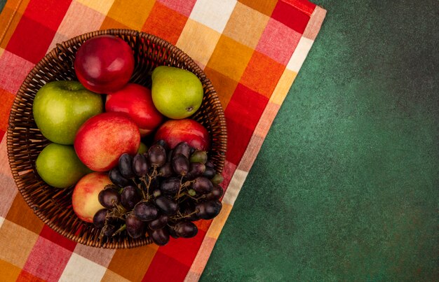 Vista superior de frutas como pêssego, maçã, uva, pêra, em, cesta, em, xadrez, pano, e, em, verde, fundo, com, cópia, space