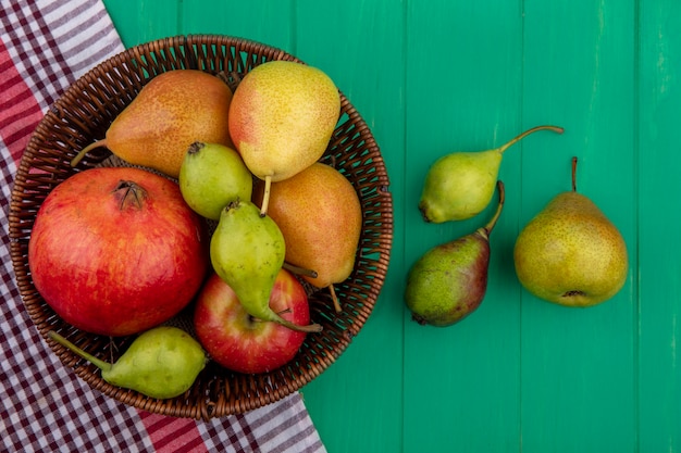 Foto grátis vista superior de frutas como romã e pêssego na cesta no pano xadrez e na superfície verde