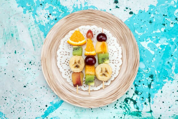 Vista superior de frutas em palitos dentro do prato na foto colorida de frutas de verão com fundo azul