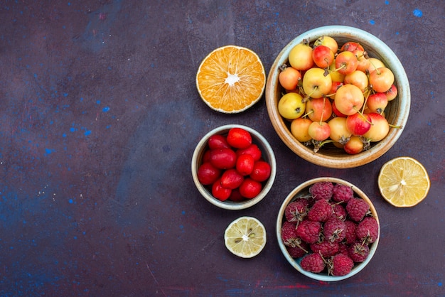 Vista superior de frutas frescas, ameixas e framboesas dentro de pratos na superfície escura