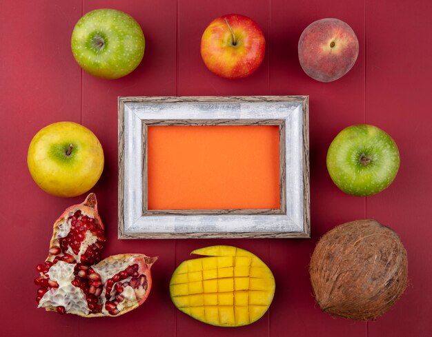 Foto grátis vista superior de frutas frescas, como fatias de manga, sementes de romã, maçãs, pêssegos e coco no vermelho