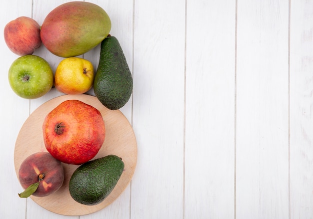 Vista superior de frutas frescas, como romã de pêssego na mesa de cozinha de madeira com abacate de maçã e manga isolado no branco