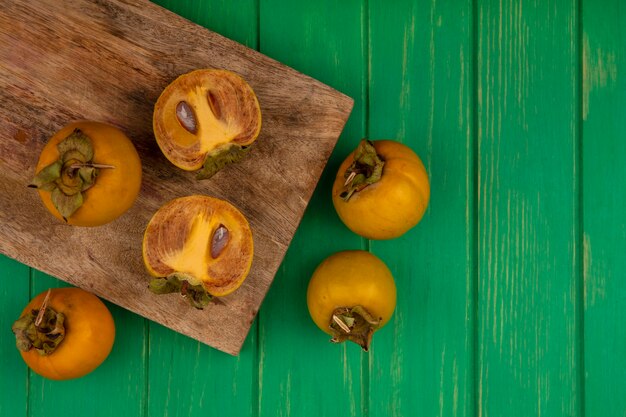 Vista superior de frutas frescas de caqui em uma placa de cozinha de madeira em uma mesa de madeira verde com espaço de cópia