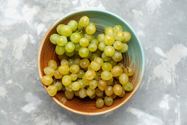 Vista superior de frutas frescas de uvas verdes dentro do prato em luz cinza, frutas suculentas maduras