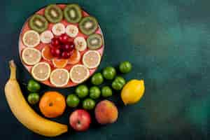 Foto grátis vista superior de frutas frescas limão tangerina banana pêssego maçã verde azedo ameixas cereja e frutas fatiadas com cerejas vermelhas no prato no escuro