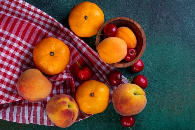 vista superior de frutas frescas maduras tangerinas pêssegos com cerejas vermelhas em tecido xadrez em verde escuro