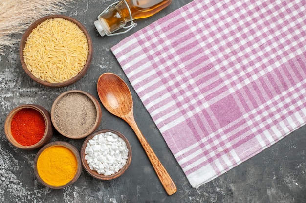 Foto grátis vista superior de fundo de cozinha com várias especiarias, colher de arroz branco cru, garrafa de óleo e toalha roxa despojada