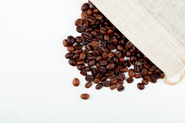 Vista superior de grãos de café torrados, espalhados de um saco em fundo branco, com espaço de cópia