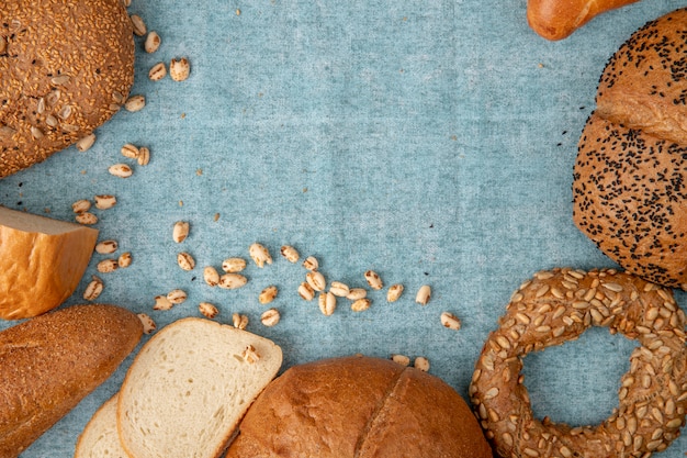 Vista superior de grãos e diferentes tipos de pão como baguete de bagel branco sobre fundo azul, com espaço de cópia