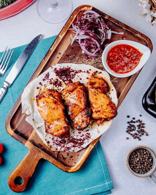 Vista superior de kebab de frango com cebolas vermelhas em uma tábua de madeira