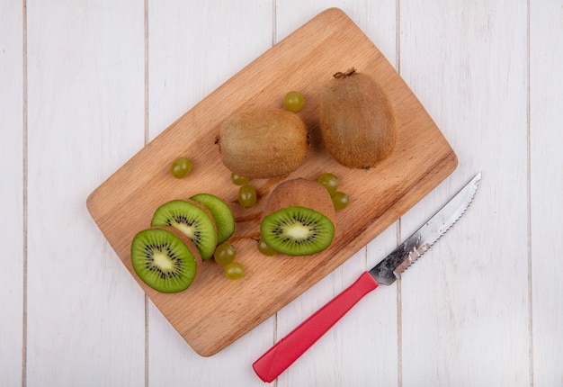 Vista superior de kiwi em uma tábua com faca na parede branca