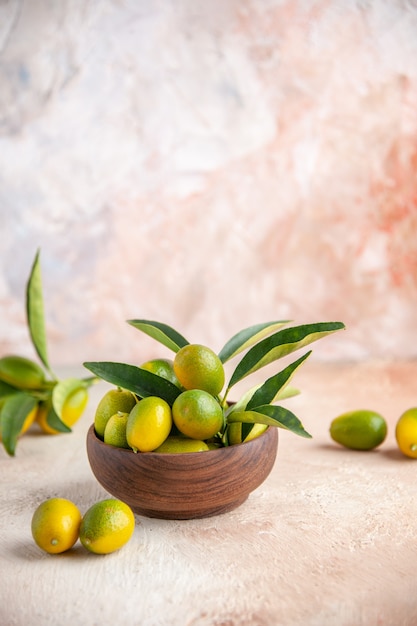 Vista superior de kumquats frescos com hastes dentro e fora de um pequeno pote de madeira em uma superfície colorida