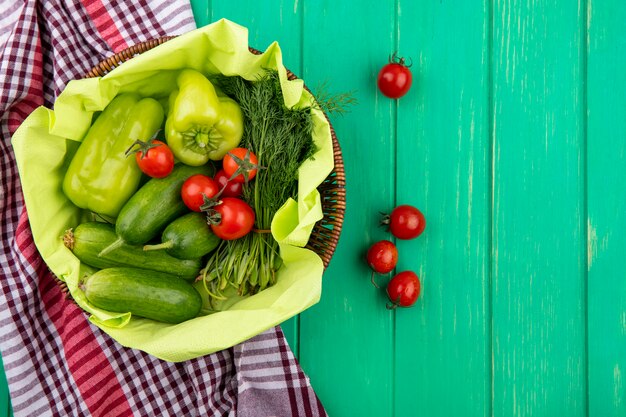 Vista superior de legumes como endro de pepino tomate pimenta na cesta no pano xadrez e superfície verde