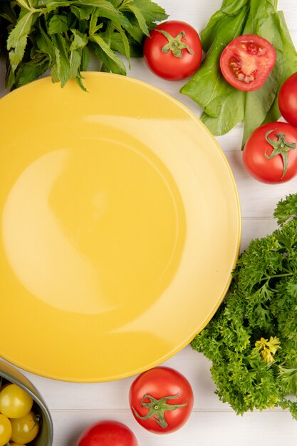 Vista superior de legumes como folhas de hortelã verde coentro tomate espinafre com prato vazio na madeira