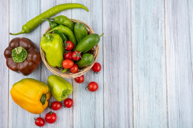 Vista superior de legumes como pimenta e pepino na cesta com tomates pimentas ao redor na superfície de madeira