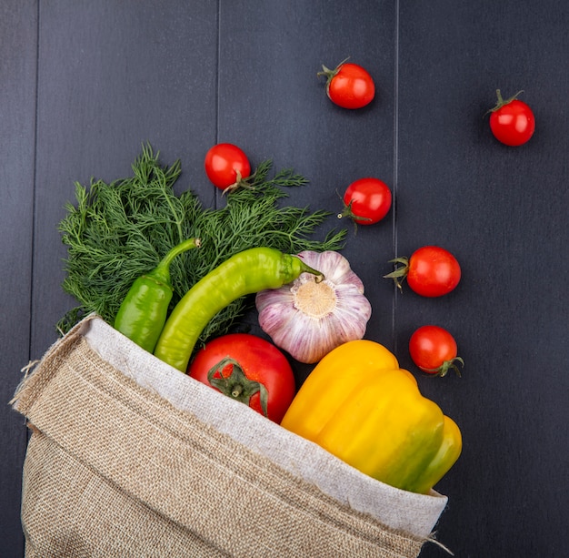 Foto grátis vista superior de legumes como pimenta tomate alho endro derramando fora do saco na superfície preta