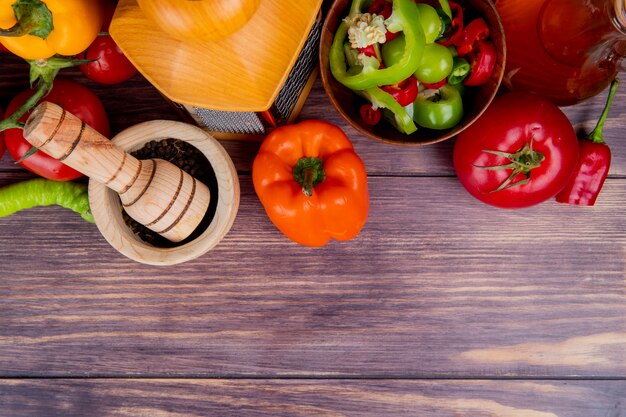 Vista superior de legumes como pimentas inteiras e fatiadas tomates inteiros com triturador de alho ralador e manteiga derretida na madeira com espaço de cópia