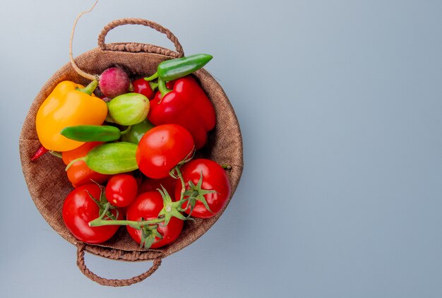 Vista superior de legumes como rabanete de tomate pimenta na cesta no lado esquerdo e fundo azul com espaço de cópia