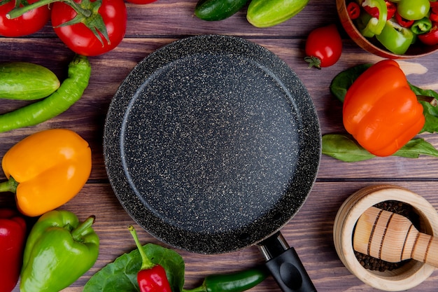 Vista superior de legumes como tomate pepino pimenta com folhas e pimenta no triturador de alho e frigideira na madeira