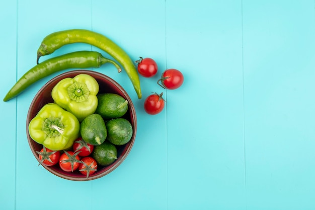 Vista superior de legumes como tomate pepino pimenta na tigela e na superfície azul