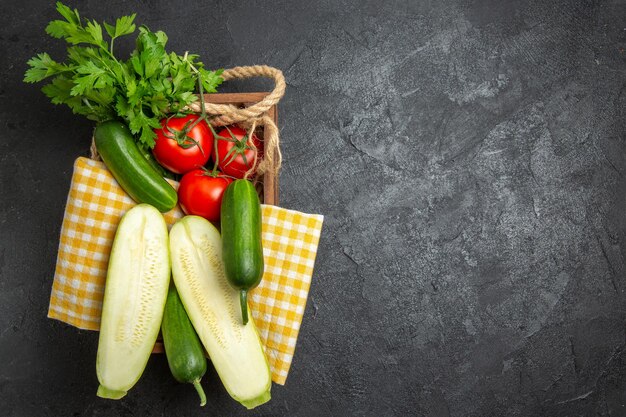 Vista superior de legumes frescos, tomates vermelhos, pepinos e abóboras com verduras na superfície cinza