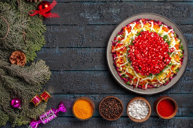 Vista superior de longe Comida de Natal Prato de Natal com tigelas de romã com especiarias e ramos de abeto com brinquedos para árvores de Natal