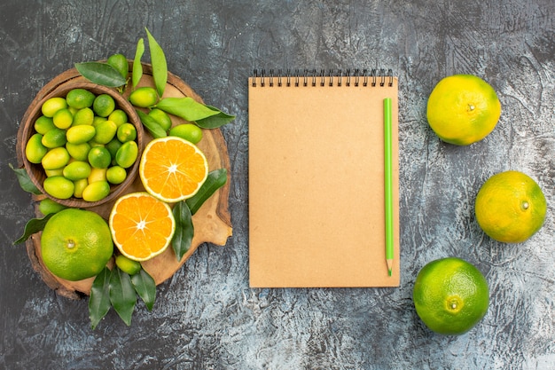 Vista superior de longe frutas cítricas laranjas tangerinas no quadro de lápis de caderno