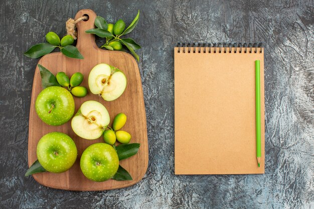 Vista superior de longe maçãs maçãs verdes frutas cítricas no quadro, caderno creme e lápis