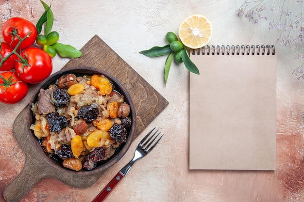 Foto grátis vista superior de longe pilaf a tábua de cortar com pilaf garfo tomate limão creme caderno