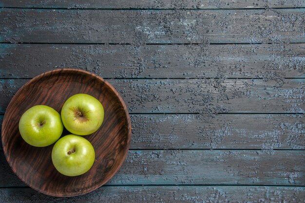 Vista superior de longe tigela de maçãs tigela marrom de apetitosas maçãs verdes no lado esquerdo da mesa escura