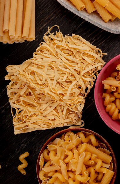 Vista superior de macaronis como tagliatelle bucatini fusilli e outros na madeira