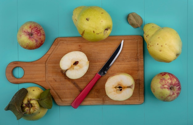 Vista superior de maçãs frescas cortadas ao meio em uma placa de cozinha de madeira com uma faca com marmelos isolado em um fundo azul